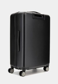 Valise noire à coque rigide avec une texture lisse, une poignée rétractable et quatre roulettes circulaires. Design minimaliste, sans logo ni motifs visibles.