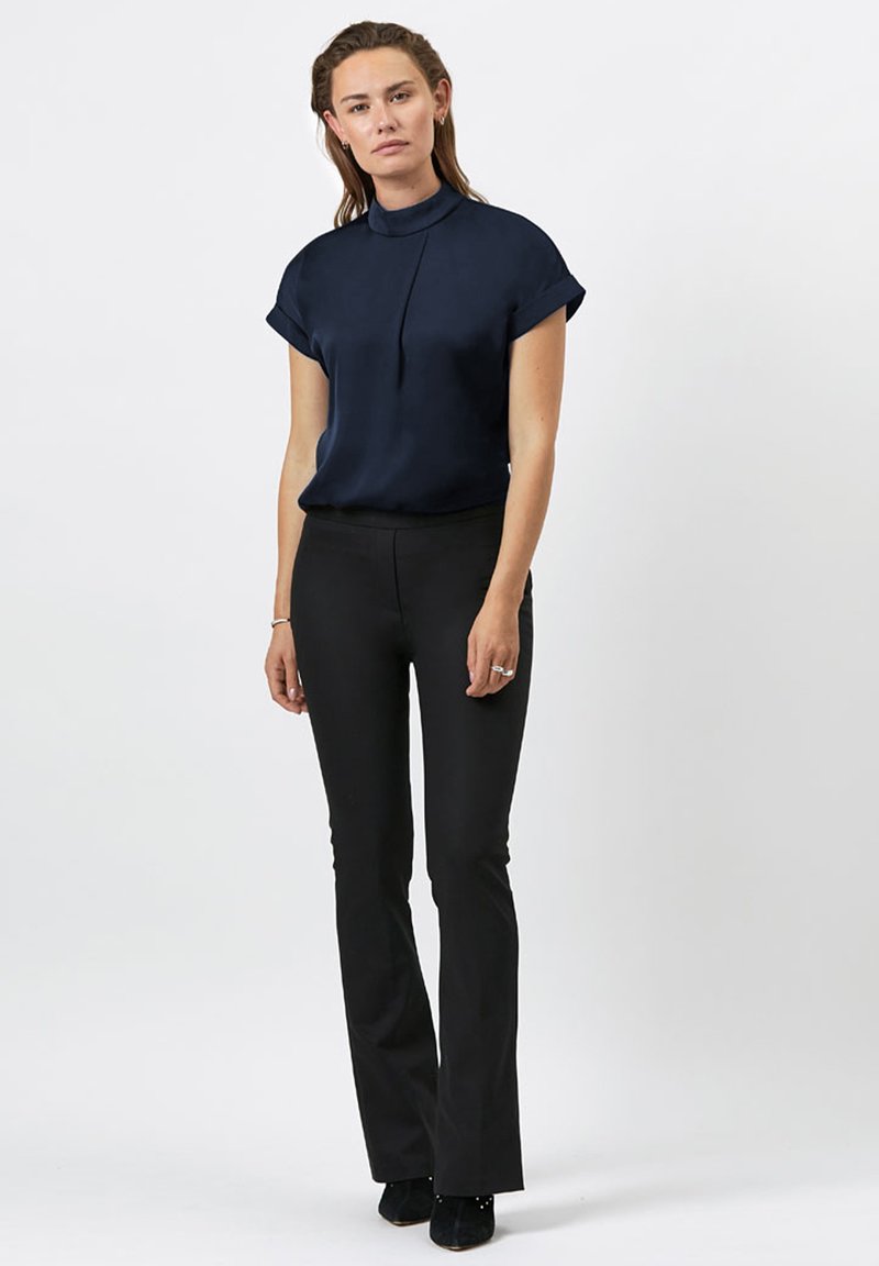 Marineblauwe blouse met korte mouwen, hoge kraag en plooidetails, gecombineerd met zwarte flared broek. Gladde textuur en nauwsluitende pasvorm.
