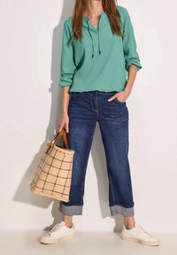 Haut à manches longues texturé couleur sarcelle avec un col en V et une capuche ; associé à un jean denim bleu foncé raccourci ; portant un sac fourre-tout en tissu à carreaux beige et des baskets blanches.