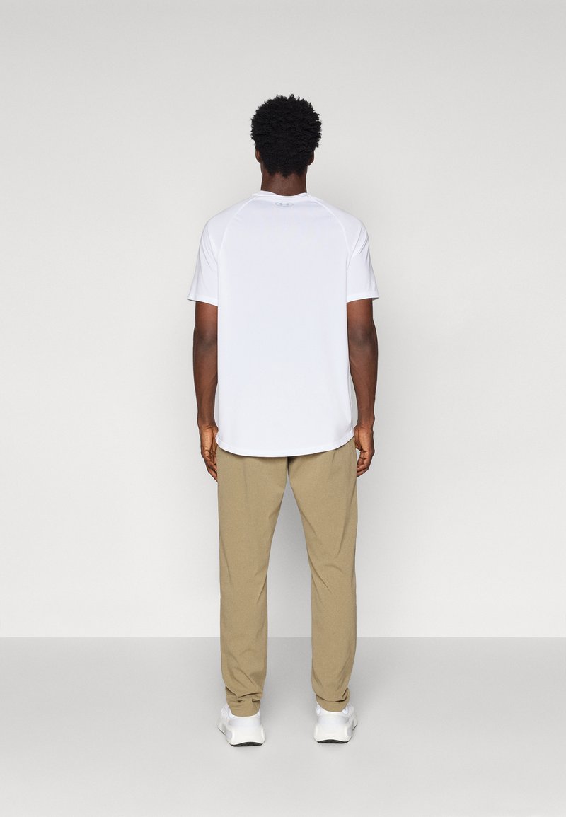 Herren T-Shirt mit kurzen Ärmeln in Weiß, mit abgerundetem Saum, kombiniert mit hellbeigen Hosen und weißen Sneakers. Schlichte Gestaltung, nahtlose Schultern.