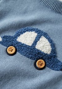 Tissu bleu tricoté avec un motif texturé de voiture bleu et blanc, présentant des roues en boutons beige cousues sur le tissu.