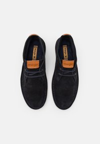 Scarpe in suede blu scuro con un'etichetta in pelle tan, design con lacci, punta rotonda e cucitura blu a contrasto. Suola piatta, due paia di occhielli.