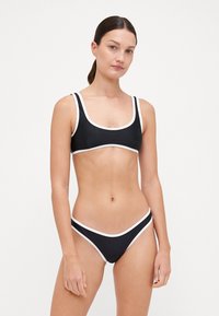 Ensemble de bikini noir avec un décolleté carré, des bordures blanches contrastantes, des bretelles ajustables et une coupe basse au niveau du bas. Texture lisse.