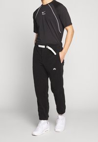 Musta urheiluasu, jossa on lyhythihainen paita valkoisilla yksityiskohdilla ja siihen sopivat mustat jogger-housut, viimeistelty valkoisella vyöllä ja lenkkareilla.