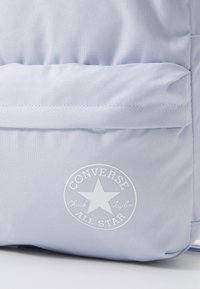Világoskék vászon hátizsák struktúrált anyagból, az elején fehér kör alakú logóval, amelyen csillag és a "CONVERSE ALL STAR" felirat található a zsebben.