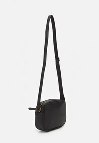 Kompakt sort læder crossbody taske med justerbar rem og guld lynlås lukning, vist mod en simpel hvid baggrund.