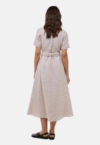 Robe en lin beige clair avec des manches courtes, une taille ceinturée et une jupe midi fluide. Présente un design simple et épuré.