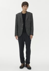 Halli tekstuuriga bleiser kahe nupuga, sobitatud musta särgi ja tumedate, lõtvade pükstega. Rinna saadud pruunid jalanõud nööpide ja lakkidega täiustavad välimust.