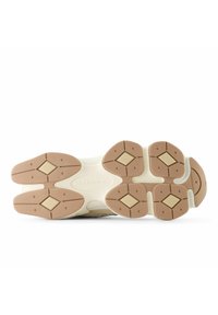 Soletta di scarpa da corsa color beige chiaro, con grip in gomma a trama, forme a diamante e una intersuola beige con dettagli del nome del marchio.