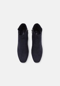 Botines de ante azul marino oscuro con una textura suave, puntera afilada y detalle de cremallera lateral. Etiqueta de tamaño visible en el interior.