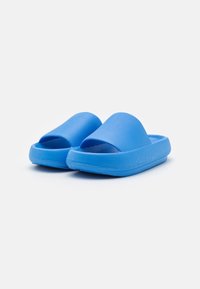 Pantofole blu senza laccio realizzate in gomma testurizzata, con design open-toe e suola spessa. Finitura liscia con un colore uniforme.