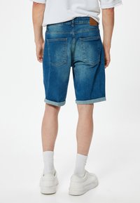 Shorts de mezclilla en azul claro con un acabado desgastado, dobladillos enrollados, dos bolsillos traseros y una etiqueta de marca de cuero marrón en la cintura.