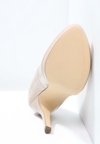 Nude lackläder högklackad sko med spetsig tå, smal stilettklack och en slät, glänsande yta. Sulan är texturerad och beige.