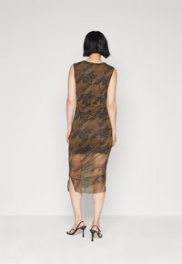 Vestido marrón transparente con patrón floral negro, diseño sin mangas y abertura lateral. Combinado con sandalias negras de tacón alto.