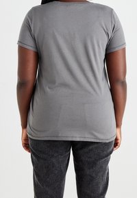 Harmaa lyhythihainen t-paita, joka on valmistettu pehmeästä materiaalista ja jossa on pyöreä pääntie. Hiukan vartaloon muotoiltu malli, jossa on ompeluyksityiskohtia helman ja hihojen kohdalla.