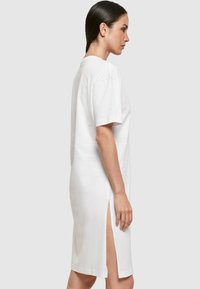 Weißes Baumwolkleid mit kurzen Ärmeln, gerader Schnitt, knielang, mit seitlichen Schlitzen für mehr Bewegungsfreiheit, glatte Textur, minimalistisches Design.