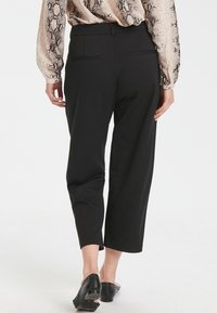 Černé zkrácené kalhoty z hladké látky, s dvěma zadními kapsami a vytvarovaným střihem, doplněné černými botami na blokovém podpatku.