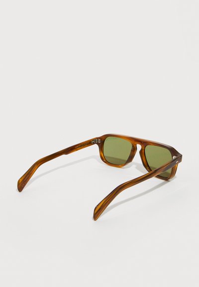 Καφέ ορθογώνια γυαλιά ηλίου με μοτίβο χελώνας και φακούς με πράσινη απόχρωση, τοποθετημένα σε λευκή επιφάνεια, με θέα από πίσω.