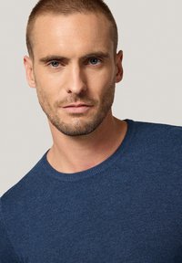 Granatowy sweter dziany z okrągłym dekoltem i teksturowanym materiałem. Zbliżenie na dekolt i górną część klatki piersiowej, podkreślające szczegółowy splot.