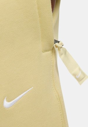Helles gelbes Sportoberteil aus strukturiertem Stoff, mit dem weißen Nike-Logo und verstellbarem seitlichen Bindeband für die Passform.