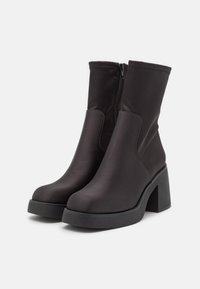Černé kotníkové boty vyrobené z hladké tkaniny, s uzávěrem na zip, blokovým podpatkem a zaoblenou špičkou se mírně zvýšenou platformou.