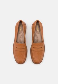 Mocassins en cuir tan à enfiler avec des accents cousus, bout rond, semelle intérieure rembourrée et détails perforés. Le logo de la marque "ALDO" est visible.
