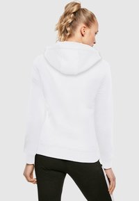 White hooded sweatshirt with a relaxed fit, featuring a kangaroo pocket, ribbed cuffs, and a soft texture. Worn with black pants.