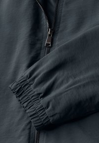 Mörkgrå jacka med texturerad tyg och elastiska ärmmuddar, försedd med en metallisk dragkedja framtill för stängning.