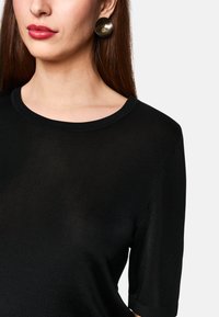 Schwarzes, geripptes Oberteil mit kurzen Ärmeln und weitem Rundhalsausschnitt, kombiniert mit glatten, glänzenden runden Ohrringen. Schlichtes, elegantes Design in figurbetontem Schnitt.