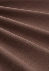 Bruine katoenstof met een gladde textuur, die subtiele plooien vertoont en een gelijkmatige kleur heeft, waarmee de stevige en zachte kwaliteiten benadrukt worden.