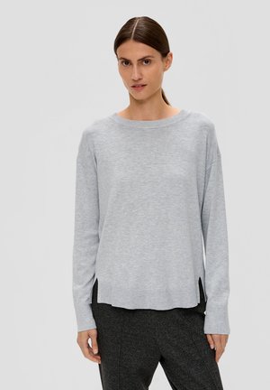 Pull à manches longues gris clair, encolure ronde, en tissu tricoté doux, fentes sur les côtés en bas, porté avec un pantalon texturé foncé.
