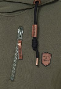 Sudadera verde con capucha que presenta un bolsillo con cierre, acentos de cuero, una capucha ajustable con cordón negro y un parche decorativo en el pecho.