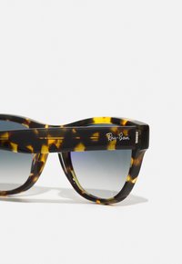 Óculos de sol Ray-Ban em tartaruga com lentes cinzas em degrade. Armação de plástico espesso com um design curvado e logótipo em relevo na haste.