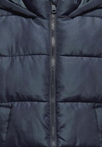 Tumši jūras spēka pūkainais mētelis ar kviltotu tekstūru, priekšējo rāvējslēdzēju un kapuci. Iezīmē horizontālas šuves un sānu kabatu.