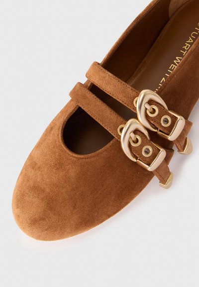Pantofii plates din suede maro au două catarame decorative din aur și un design tăiat deschis în partea din față. Textură netedă și vârf rotunjit.