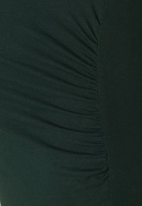 Mörkgrön tyg med samlade texturer längs ena sidan, som visar ett slätt och elastiskt material. Designen framhäver subtila åsar.