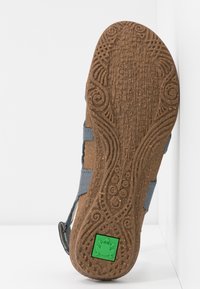 Semelle en caoutchouc brun avec des motifs texturés et un logo de grenouille verte ; dessus gris avec des sangles et un design décontracté.