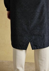 Tunic navy con motivo floreale e leggero spacco sull'orlo, abbinata a pantaloni chiari. Il tessuto sembra liscio e morbido.