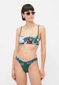To-delt bikinisett med trykt bandeau-topp med tynne grønne stropper og en lavtsittende bunn i mørkegrønn med teksten "SURF ALL DAY".