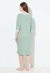 Vestito da notte verde a lunghezza ginocchio realizzato in tessuto morbido, con maniche di tre quarti impreziosite da dettagli a righe rosa e bianche sui polsi e sul collo.