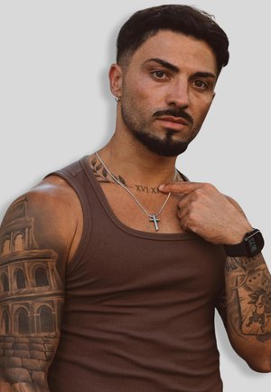 Braunes geripptes Tanktop, silberne Kreuzkette, Tätowierungen an den Armen, einschließlich einer, die ein Gebäude darstellt, helle Haut, dunkles Haar und eine Uhr.