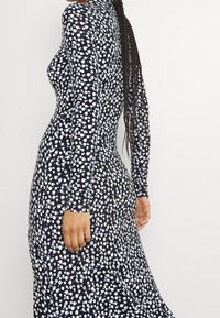 Mörkblå långärmad klänning i svart tyg med vita och blåa prickar. Slimmad passform med rund halsringning och mjuk textur.