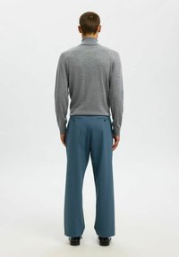 Siv turtleneck pulover v kombinaciji z modrimi širokimi hlačami. Obleka ima gladko teksturo in gumbaste zadnje žepke.