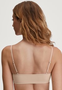 Reggiseno beige senza cuciture con spalline regolabili. Tessuto liscio, design semplice, dotato di chiusura a gancetto sul retro. Senza imbottitura o decorazioni.