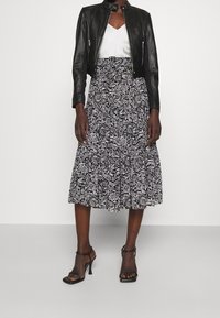 Veste en cuir noire cropped, top en V blanc, jupe midi à motif floral en noir et blanc, avec des sandales à talons.
