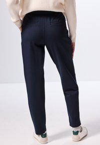 Pantaloni navy visti da dietro, con due tasche posteriori, una vestibilità dritta e una texture del tessuto liscia abbinati a sneakers bianche.