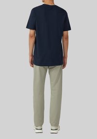 Granatowa bawełniana koszulka z okrągłym dekoltem, zestawiona z jasnobrązowymi spodniami. Tkanina wydaje się miękka z lekkim rozciąganiem. Białe trampki dopełniają stylizację.