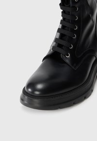 Bottines noires en cuir avec empeigne lacée, bout rond et semelle texturée. Présentent des œillets en métal argenté et une finition lisse et polie.