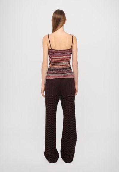 Top multicolor fără mâneci, cu bretele subțiri, având dungi orizontale. Asortat cu pantaloni înalți de culoare maro închis, cu un model în zigzag.