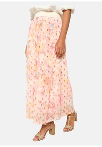 Jupe maxi florale rose en tissu texturé, ornée de motifs à pois dorés et dotée d'une ceinture élastique, accompagnée de sandales à talons blocs dorés.